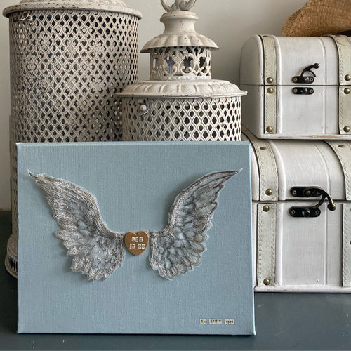 Personalised embroidered wings on a duck egg blue canvas with a wooden heart featuring names, dates, or quotes.